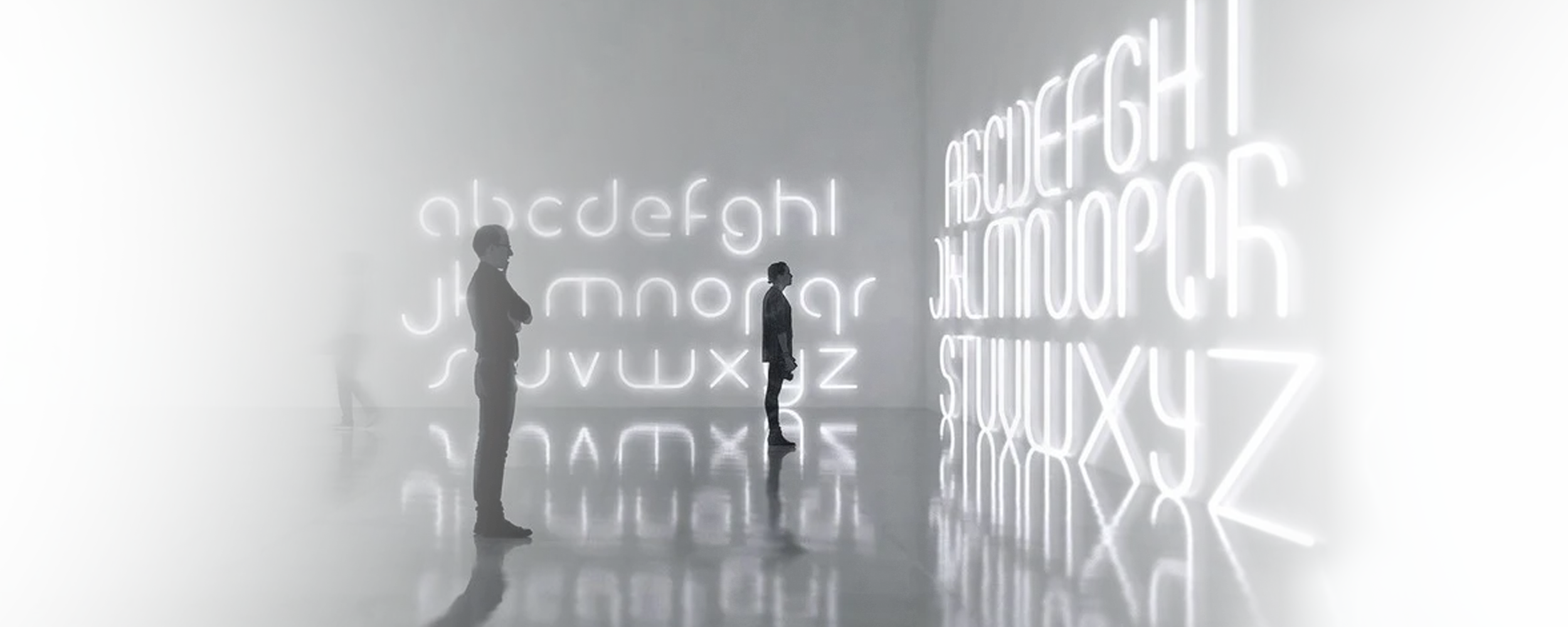 2 hommes en train de regarder un mur de lettres de l'alphabet lumineuses